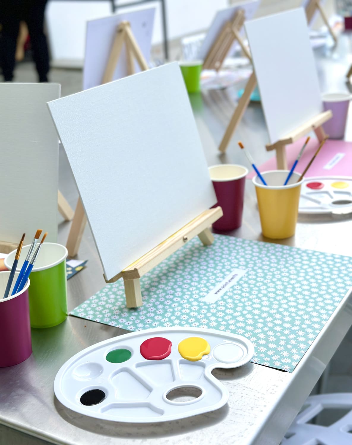 Brushes, paint cups and a blank canvas laid out on a prepared table