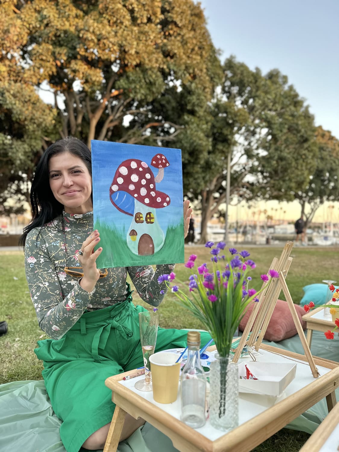 A guest holding up a finished painting at an outdoor picnic session