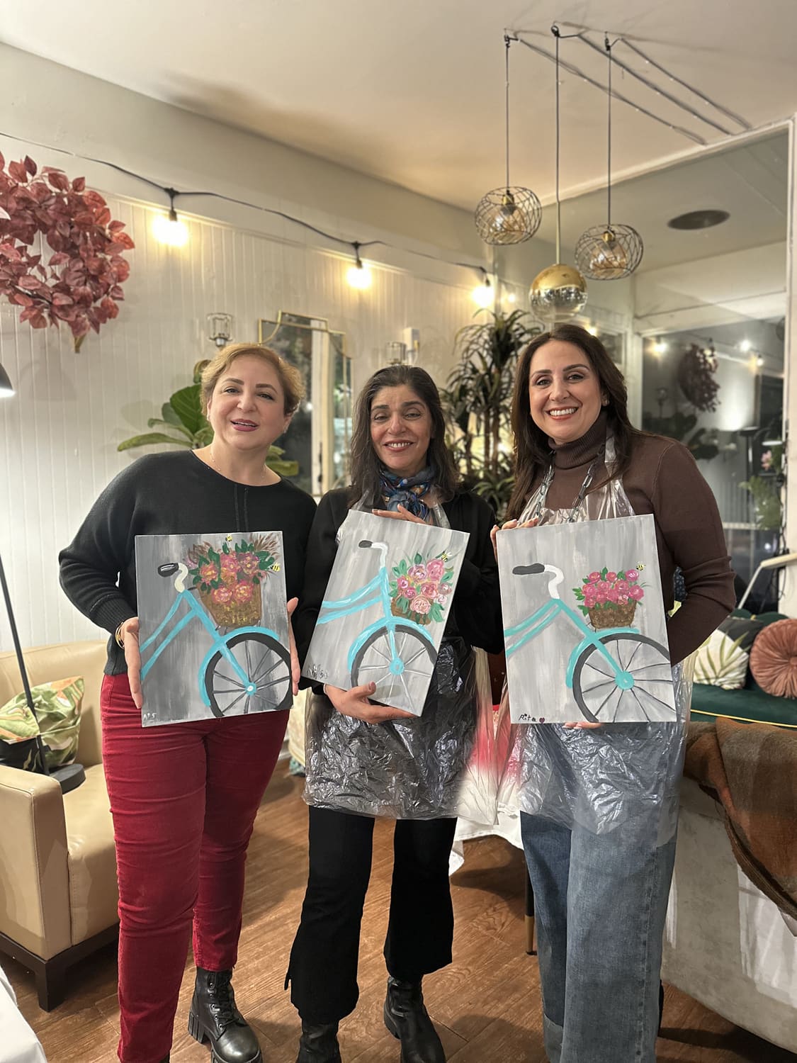 Three guests holding up the bicycle paintings they finished together