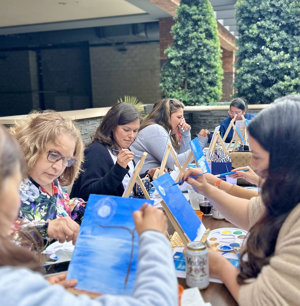 A company team painting side by side at long outdoor tables