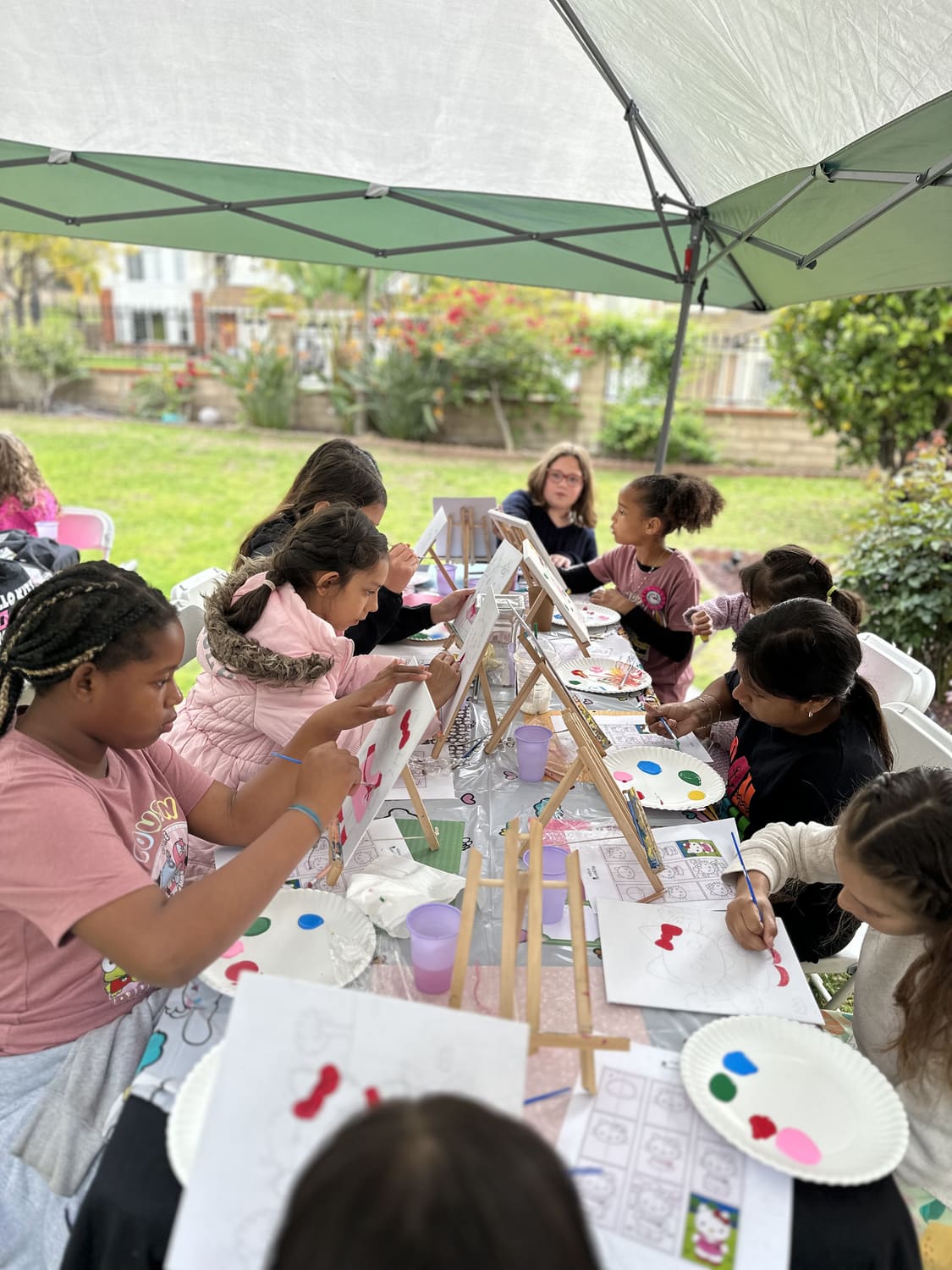 Children painting together at a long table set up on a lawn