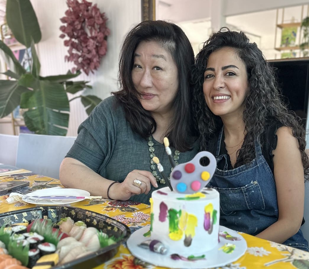 Nasim Askar celebrating with a guest beside a birthday cake decorated as a paint palette
